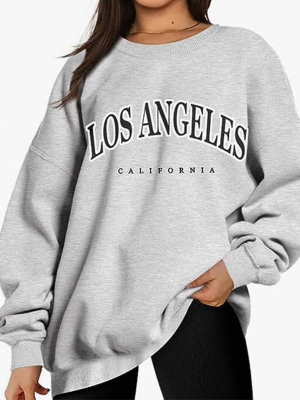 A model wearing an oversized light gray sweatshirt with 'LOS ANGELES CALIFORNIA' text graphic, paired with black leggings on white background