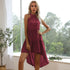 A woman with blonde hair is wearing a burgundy halter neck tiered dress and posing with one hand on her hip by a window