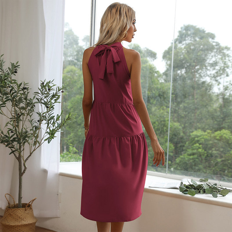 A woman with blonde hair is wearing a burgundy dress, showing the back bow detail while standing near plants