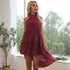 A woman with blonde hair is wearing a burgundy halter dress and standing with one hand near her hip by a window