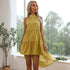 A woman with blonde hair is wearing a yellow halter neck dress and standing by a window with decorative plants