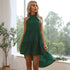 A woman with blonde hair is wearing an emerald green halter dress and standing near a window with plants