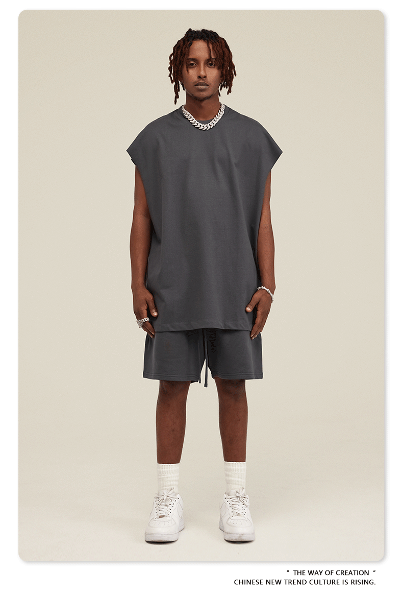 Male model in dark gray matching set with oversized muscle tee, drawstring shorts and silver chain necklace