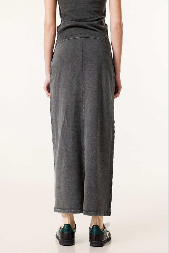 Rear view of long dark gray denim skirt with center back seam, worn with black and gray sneakers and cream socks