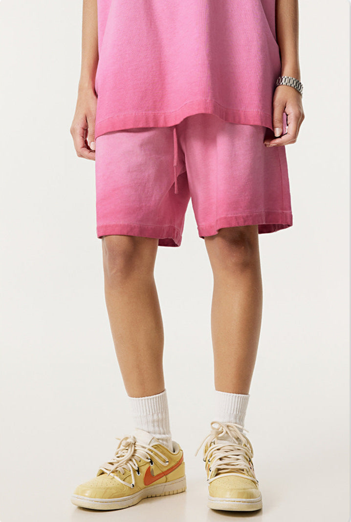 A person wearing bright pink washed cotton shorts with matching top and cream athletic shoes against white background