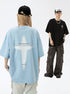 A man and woman are standing against a white backdrop. She wears light blue tee with cross graphic, he wears black tee with cross emblem and white trucker hat