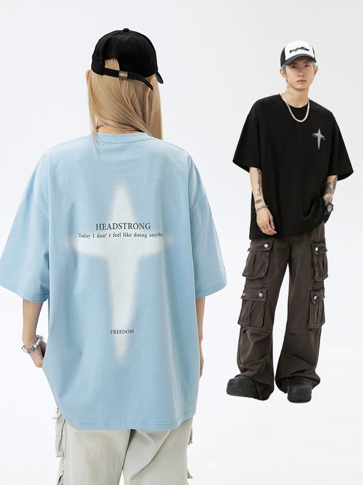 A man and woman are standing against a white backdrop. She wears light blue tee with cross graphic, he wears black tee with cross emblem and white trucker hat