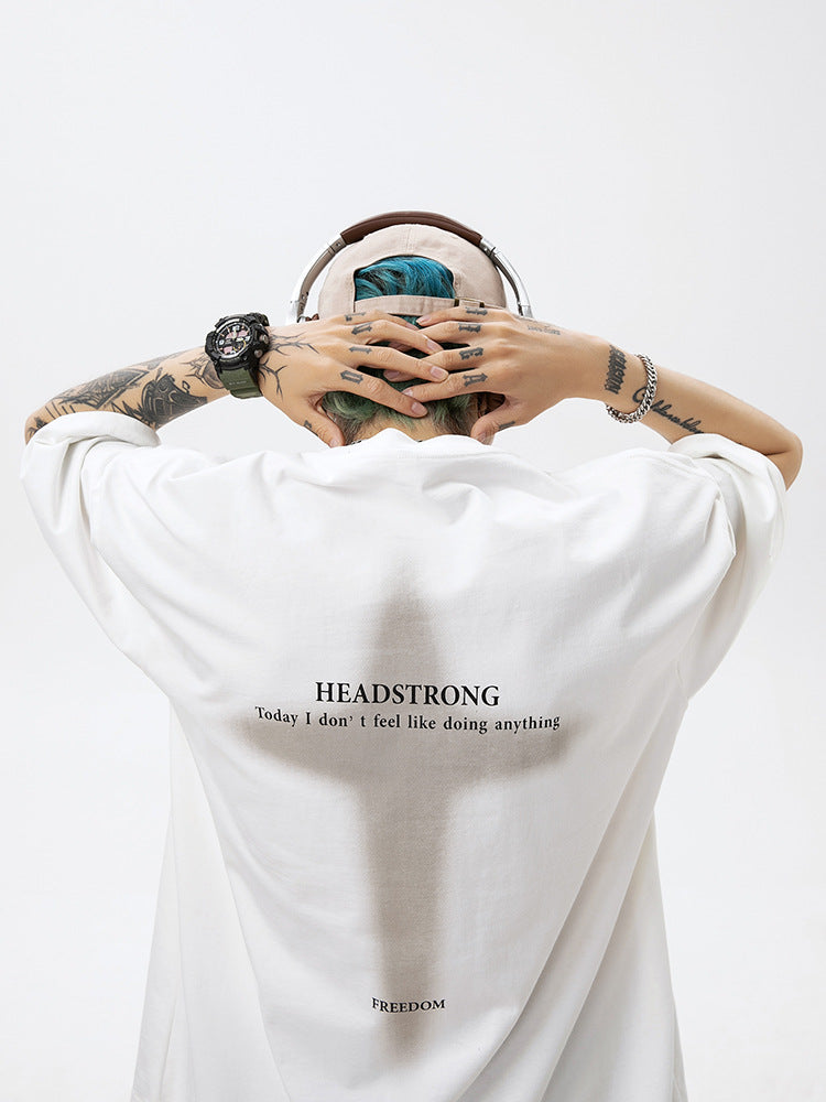 A man is shown from behind wearing white oversized tee with headphones. Blue-green hair visible, tattoo-covered arms and "HEADSTRONG" text with cross design on back