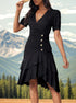 A woman wearing a black wrap dress with button detail and layered ruffle hem poses outdoors against a mountain backdrop