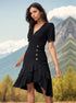 A woman in a black V-neck dress with puff sleeves and asymmetrical ruffle hem stands in front of mountain scenery