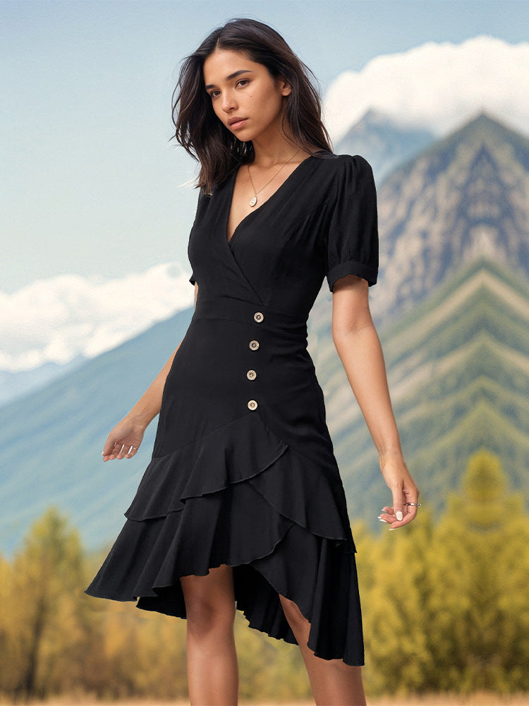 A woman in a black V-neck dress with puff sleeves and asymmetrical ruffle hem stands in front of mountain scenery