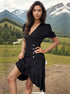 A woman posing with hand on hip in a black button-front dress with tiered ruffle hem against scenic mountain valley background