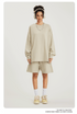 Woman in beige sweatshirt and shorts set with headphones, necklace, white socks and sneakers