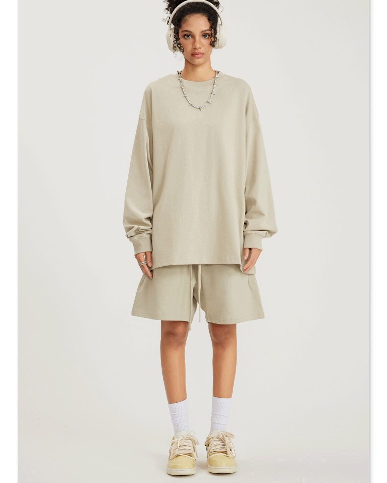 Woman in beige sweatshirt and shorts set with headphones, necklace, white socks and sneakers