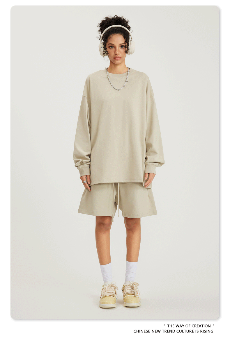 Woman in beige sweatshirt and shorts set with headphones, necklace, white socks and sneakers