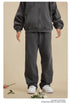 Front view of person in dark grey sweatsuit with relaxed fit pants and white sneakers on beige background