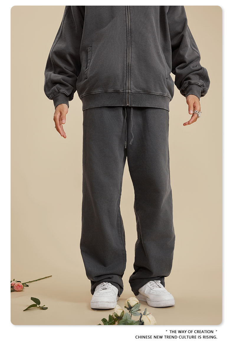 Front view of person in dark grey sweatsuit with relaxed fit pants and white sneakers on beige background