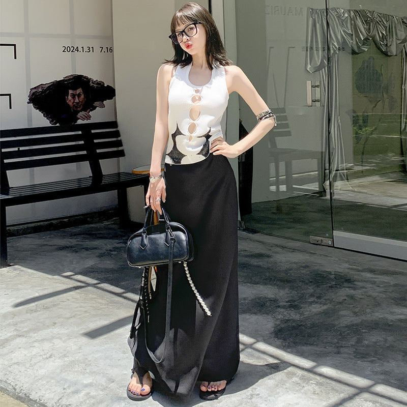 Woman in white cut-out top and black maxi skirt, wearing glasses, standing in an indoor setting with cars visible outside