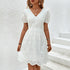 White eyelet lace dress with puff sleeves and a V-neckline, styled with gold jewelry against a white textured background