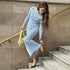Woman in powder blue ribbed dress adjusting heel on concrete stairs, carrying pastel yellow handbag, urban fashion