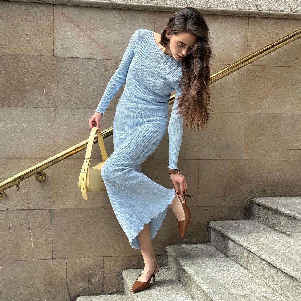 Woman in powder blue ribbed dress adjusting heel on concrete stairs, carrying pastel yellow handbag, urban fashion