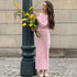 Long pink ribbed dress styled with sneakers and yellow spring flowers, casual street style against architectural column