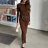 Brown ribbed maxi dress with wide belt and cream handbag, styled against library bookshelf backdrop