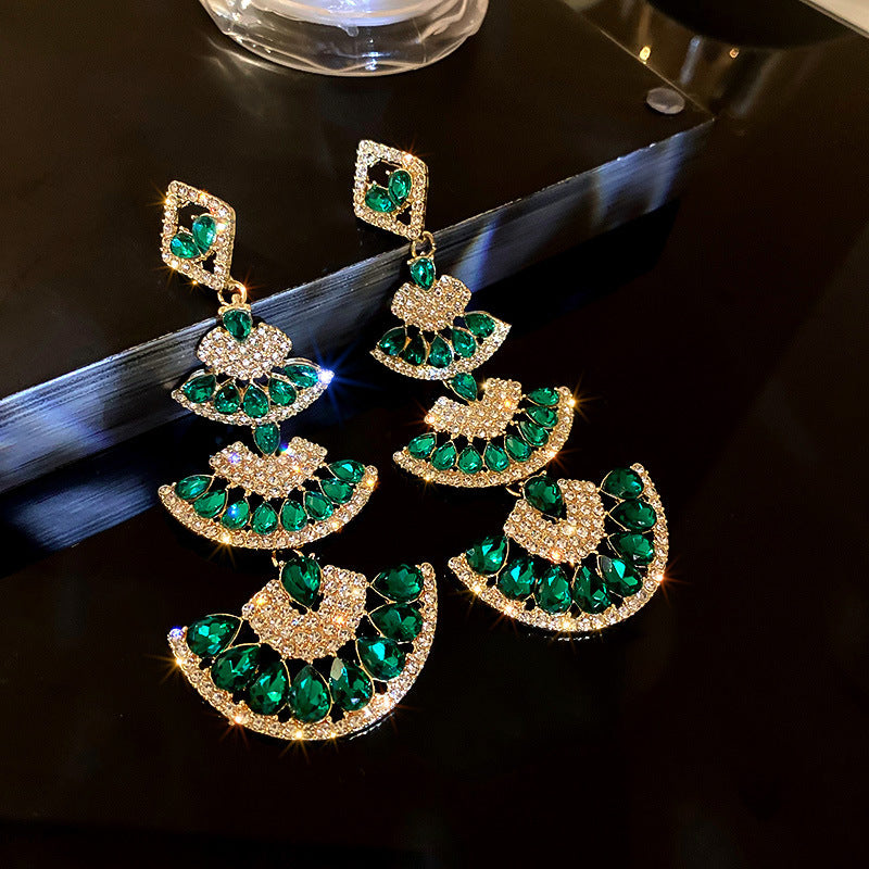 Luxurious gold statement earrings with a cluster of green crystal beads and a central emerald-cut stone, creating a dramatic drop effect