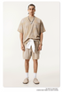 Model in beige t-shirt and shorts with silver necklace, white accent and loafers against cream background