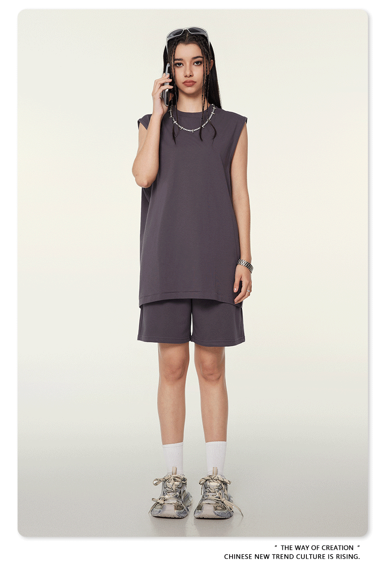 Model talking on phone wearing dark gray sleeveless top and shorts set, silver chain necklace and sunglasses on neutral background