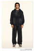 Model with twisted braids wearing black sweatsuit set with hoodie and wide-leg pants against cream background