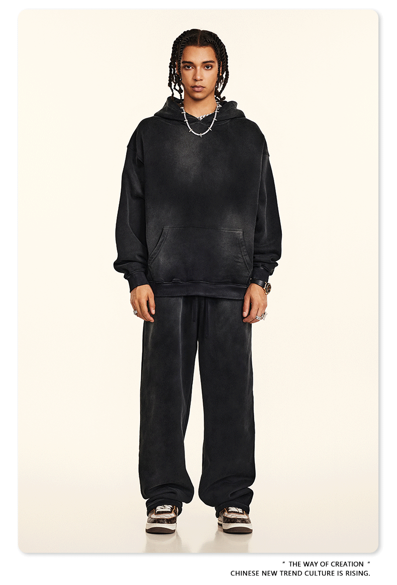 Model with twisted braids wearing black sweatsuit set with hoodie and wide-leg pants against cream background