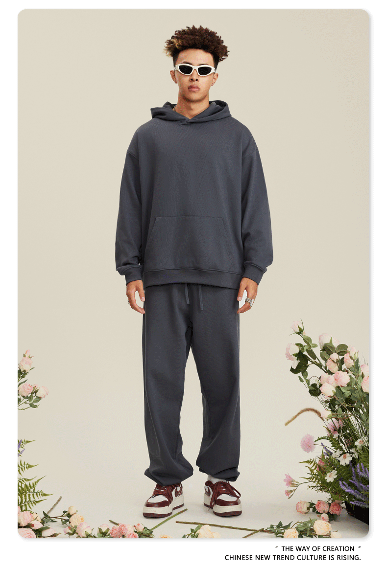 Man wearing charcoal gray hoodie and matching sweatpants with white sunglasses against floral background