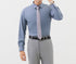 A model is wearing a steel blue dress shirt with gray tie and light gray trousers. Hand touching watch while other in pocket