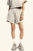 A woman's lower body in cream colored shorts with elastic waistband, white socks and chunky sneakers against white background