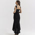 A model is posing with back towards camera wearing a black lace formal dress with ruched detail and high-low hemline against white background
