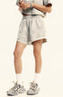 A woman with hands clasped wearing cream colored loungewear set with crop top, shorts, white socks and sneakers