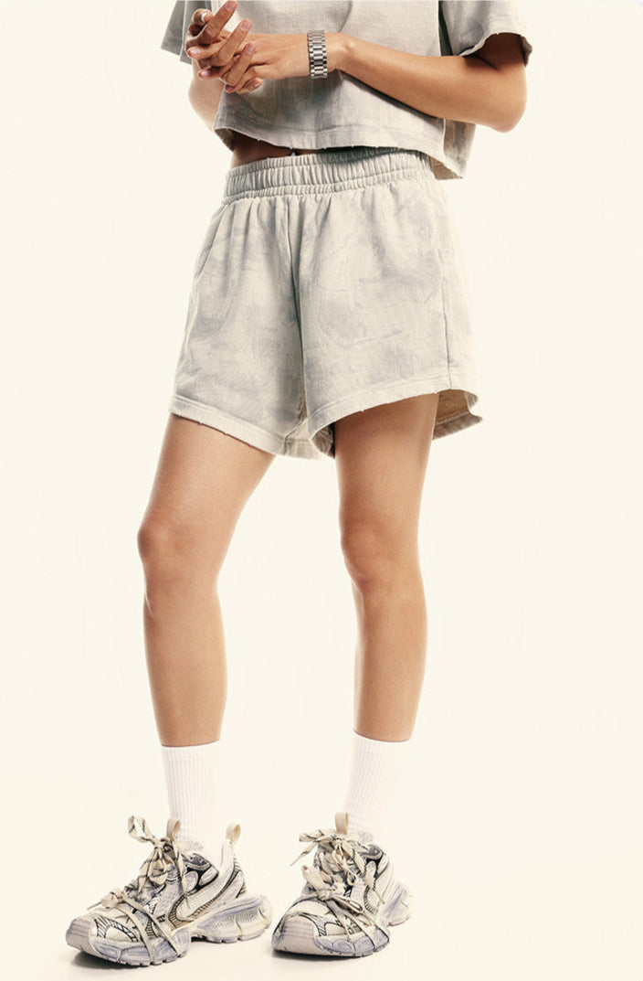 A woman with hands clasped wearing cream colored loungewear set with crop top, shorts, white socks and sneakers