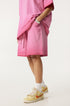 A side view of a person wearing bright pink washed cotton shorts with silver watch and cream athletic shoes