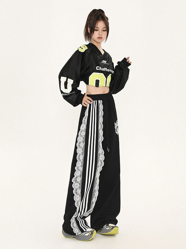 Side angle of model in black cropped athletic jersey, oversized wide-leg pants with contrast white lace trim and triple stripe detail, yellow and gray sneakers