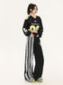 Model posing in black cropped sports jersey with neon yellow '08' numbering, high-waisted wide pants with white lace trim detail, hands at waist, minimalist background