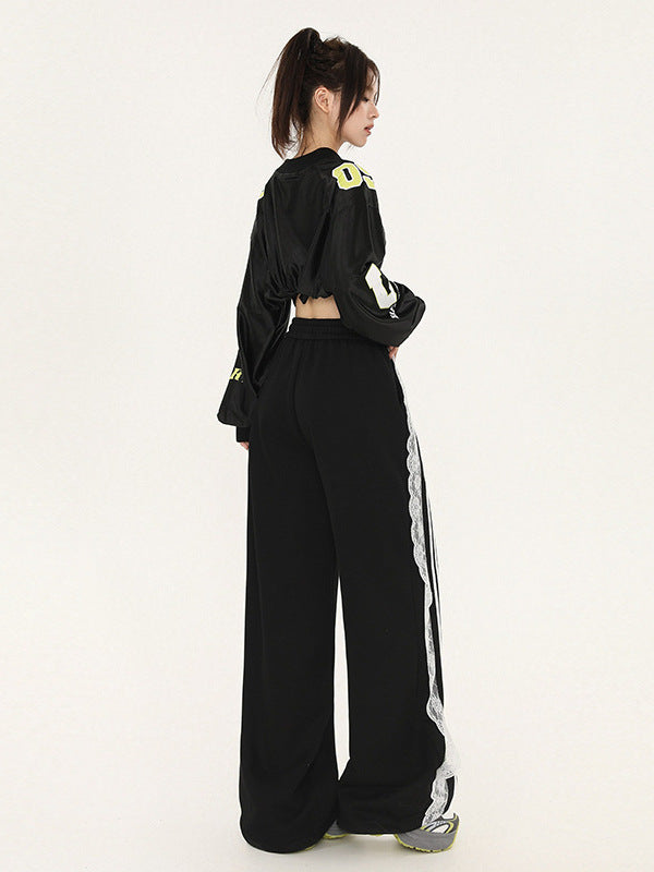 Back view of model with ponytail wearing cropped black jersey with yellow numbers, wide-leg pants featuring white lace trim and sporty stripes, streetwear aesthetic
