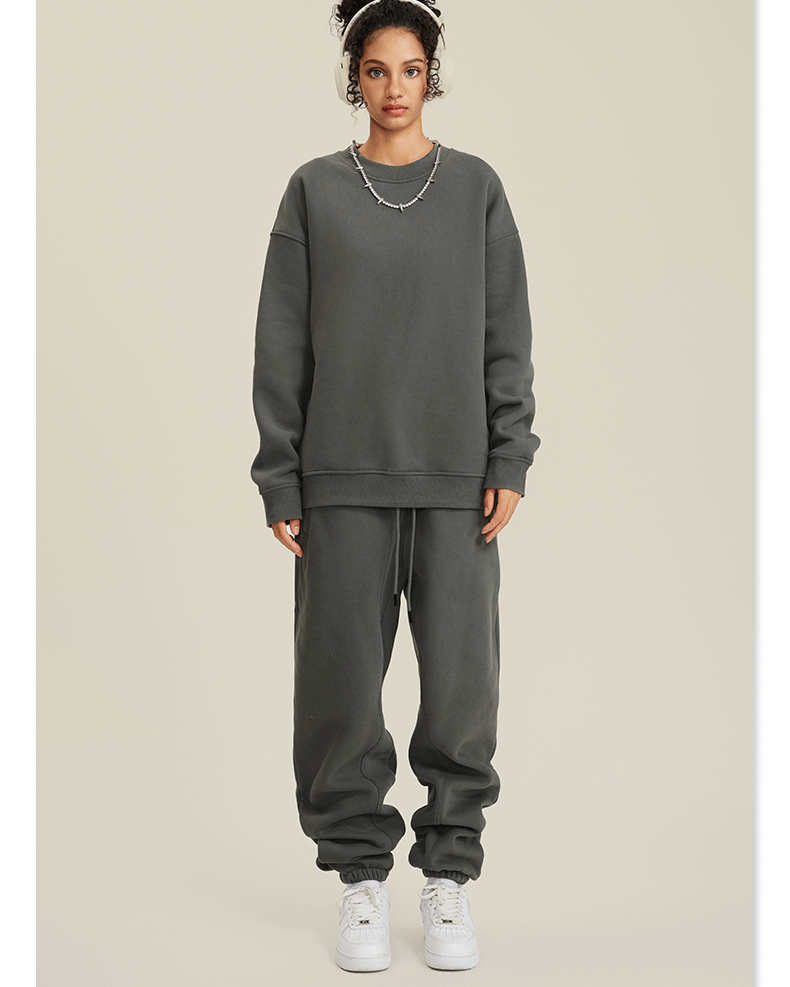 Model in olive green sweatsuit set with crew neck sweatshirt and matching joggers, styled with white headband and silver necklace