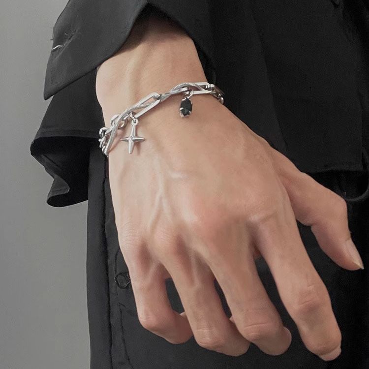 Silver chain bracelet with cross and black gemstone charms, worn on a wrist with a black shirt for a stylish, edgy look.