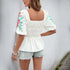 Back view of a white smocked blouse with puff sleeves and embroidered floral details, styled with denim shorts.