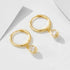 Gold mini hoop earrings with dangling teardrop crystal charms photographed on white minimalist surface