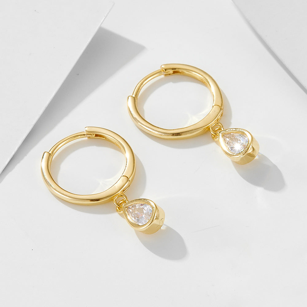Gold mini hoop earrings with dangling teardrop crystal charms photographed on white minimalist surface