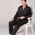 Man seated in white chair wearing black silk pajamas with contrast piping and button-front top