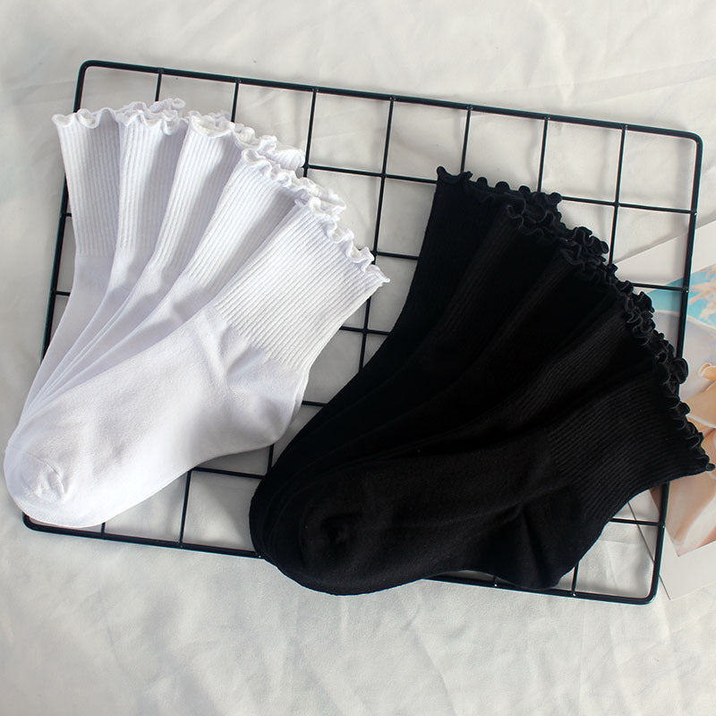 White and black ruffle-edge socks arranged on a black metal grid display against white background, showing decorative frilled trim detail