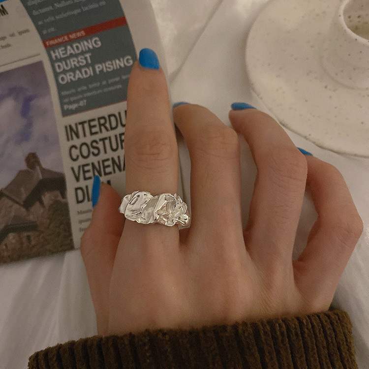 Hand with blue nails wearing textured silver ring, reading a book or magazine in the background